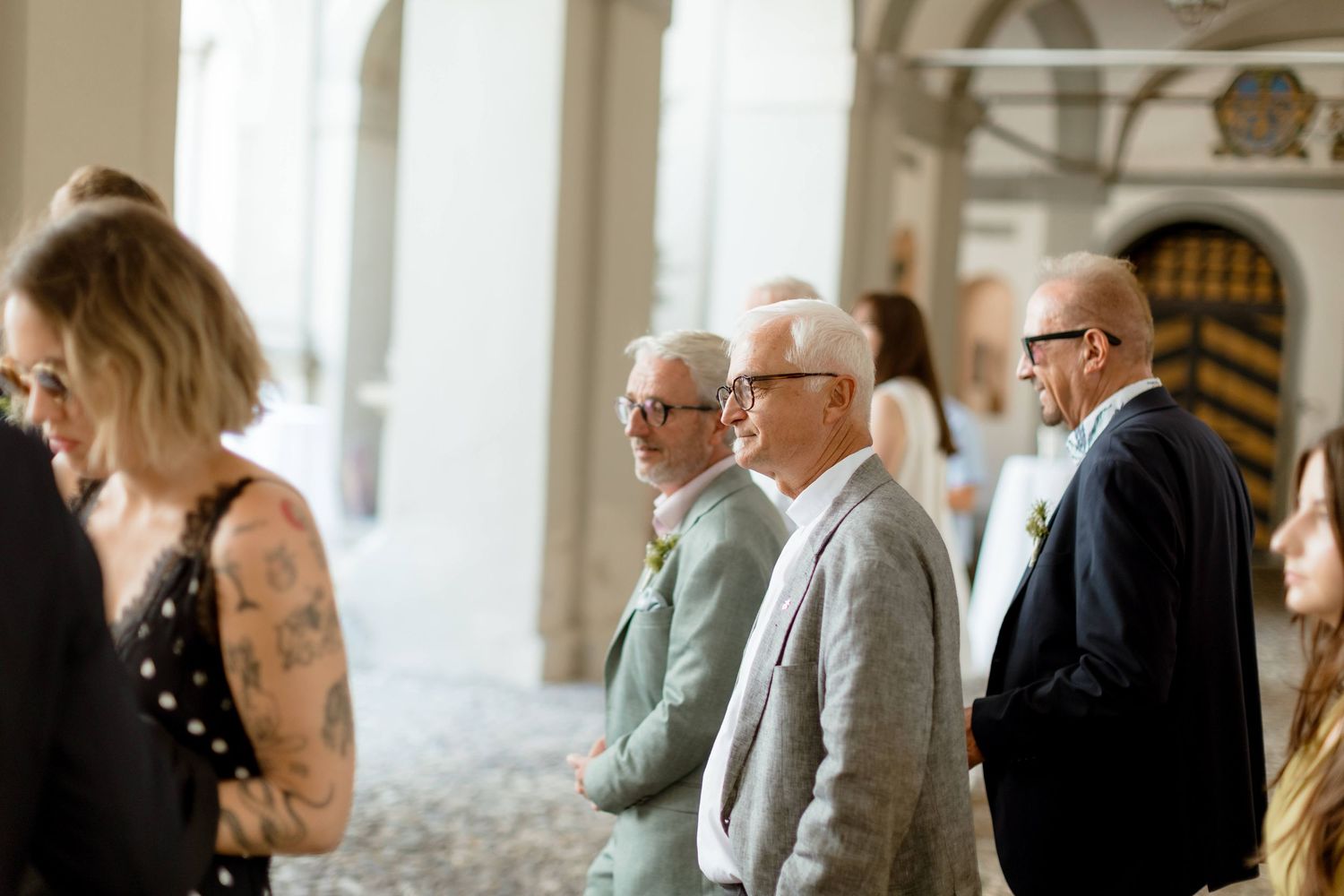 Elegantly dressed wedding guests mingling under an archway at a formal outdoor wedding reception.