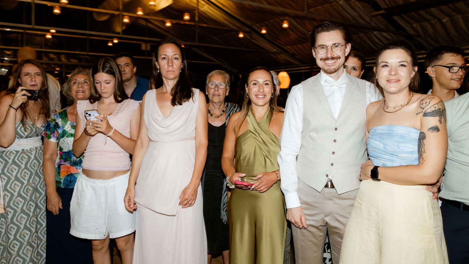 Group of wedding guests posing together smiling at an indoor reception venue.