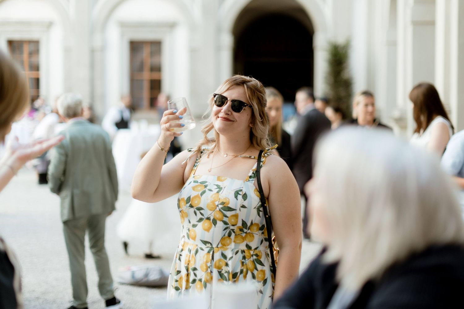 Wedding guest in yellow floral dress taking a selfie outdoors at a elegant venue celebration.