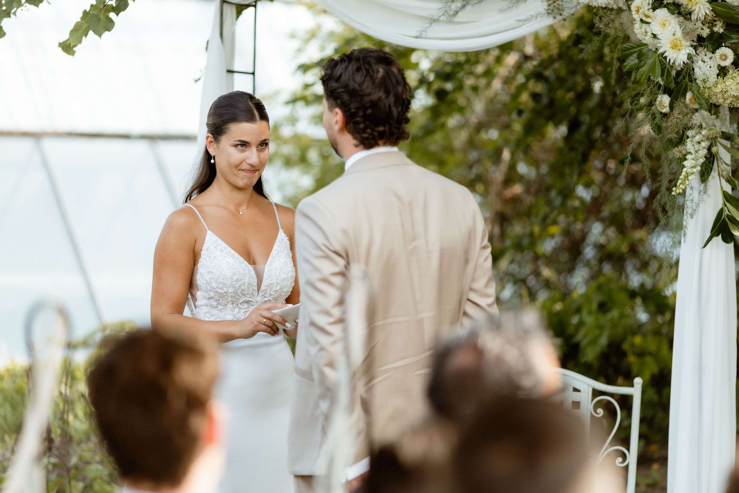 Bride smiling at groom during outdoor wedding ceremony with floral arch.
