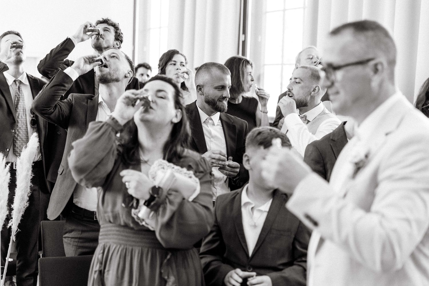 Black and white photo of wedding guests taking shots together during a joyful reception toast.