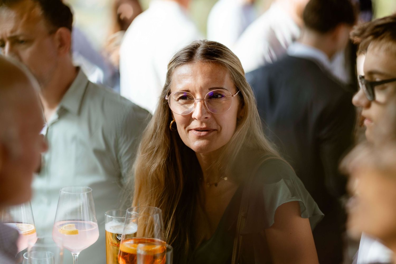 Elegant woman with long hair and glasses at a wedding reception holding a cocktail glass.