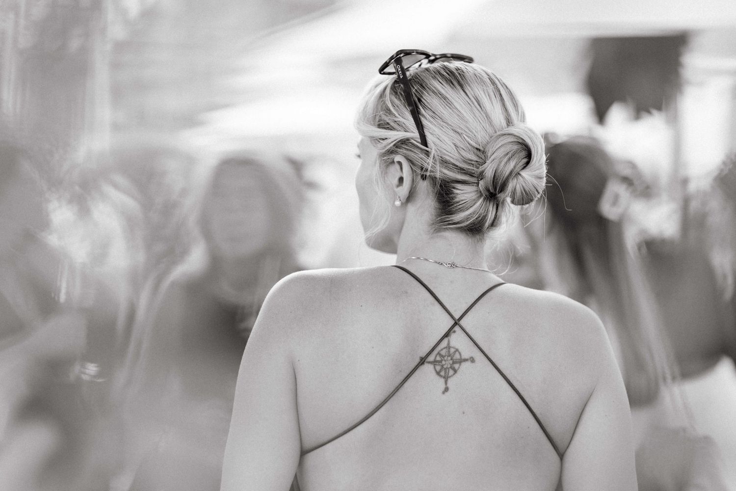 Black and white photo of blonde woman with updo and cross tattoo on her back.