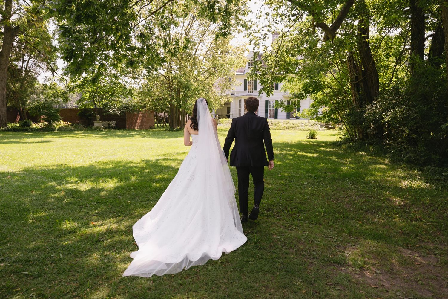 Bride and groom holding hands while walking away across the lawn toward Wadsworth Homestead in Geneseo, NY.