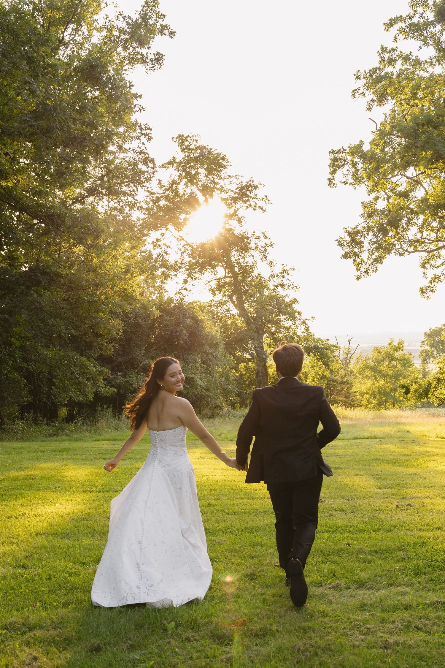 Bride looking back smiling while holding hands and running with groom at golden hour at Wadsworth Homestead in Geneseo, NY.