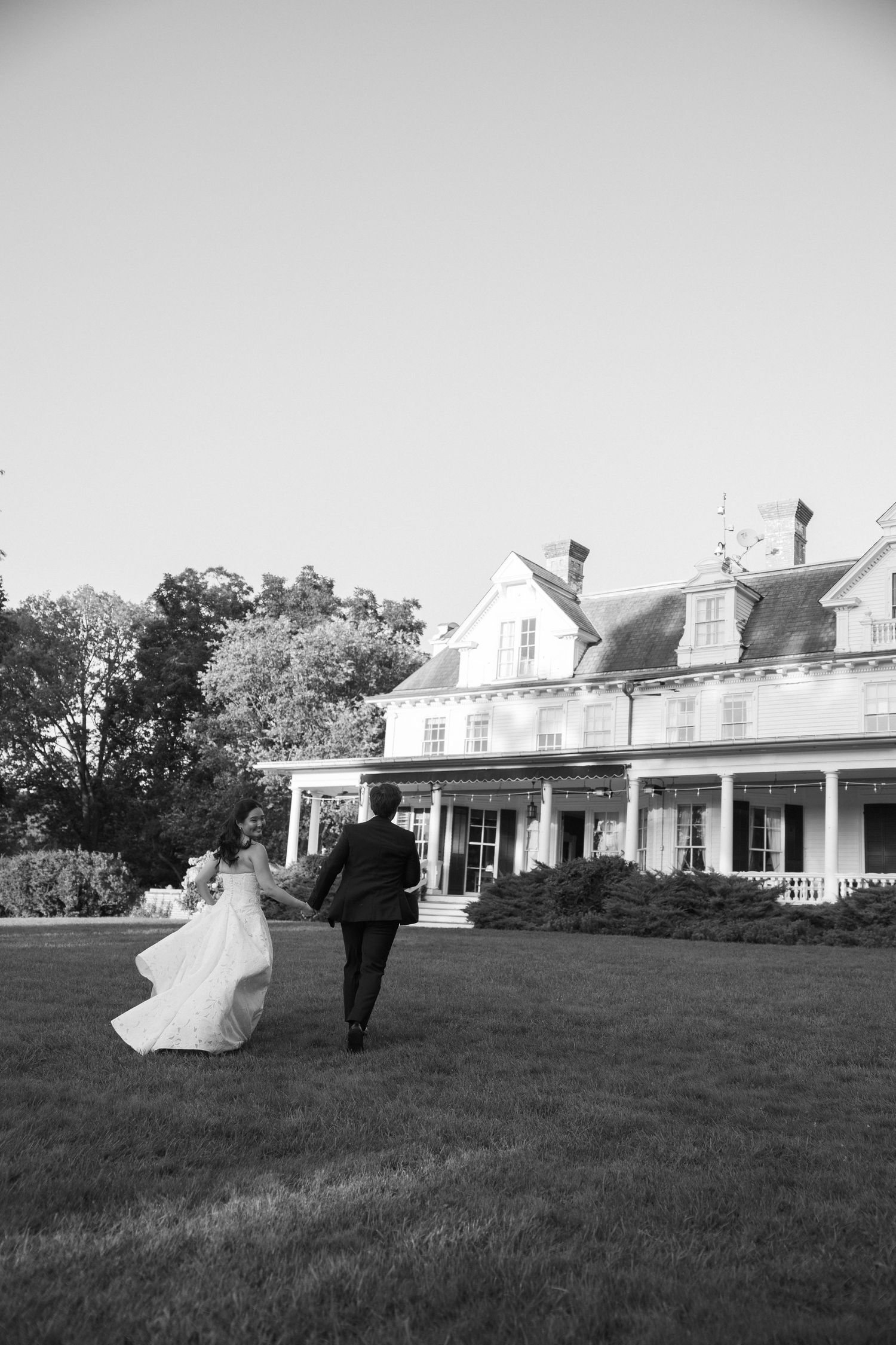 Black and white photo of bride and groom running towards Wadsworth Homestead in Geneseo, NY, by Upstate NY wedding photographer.