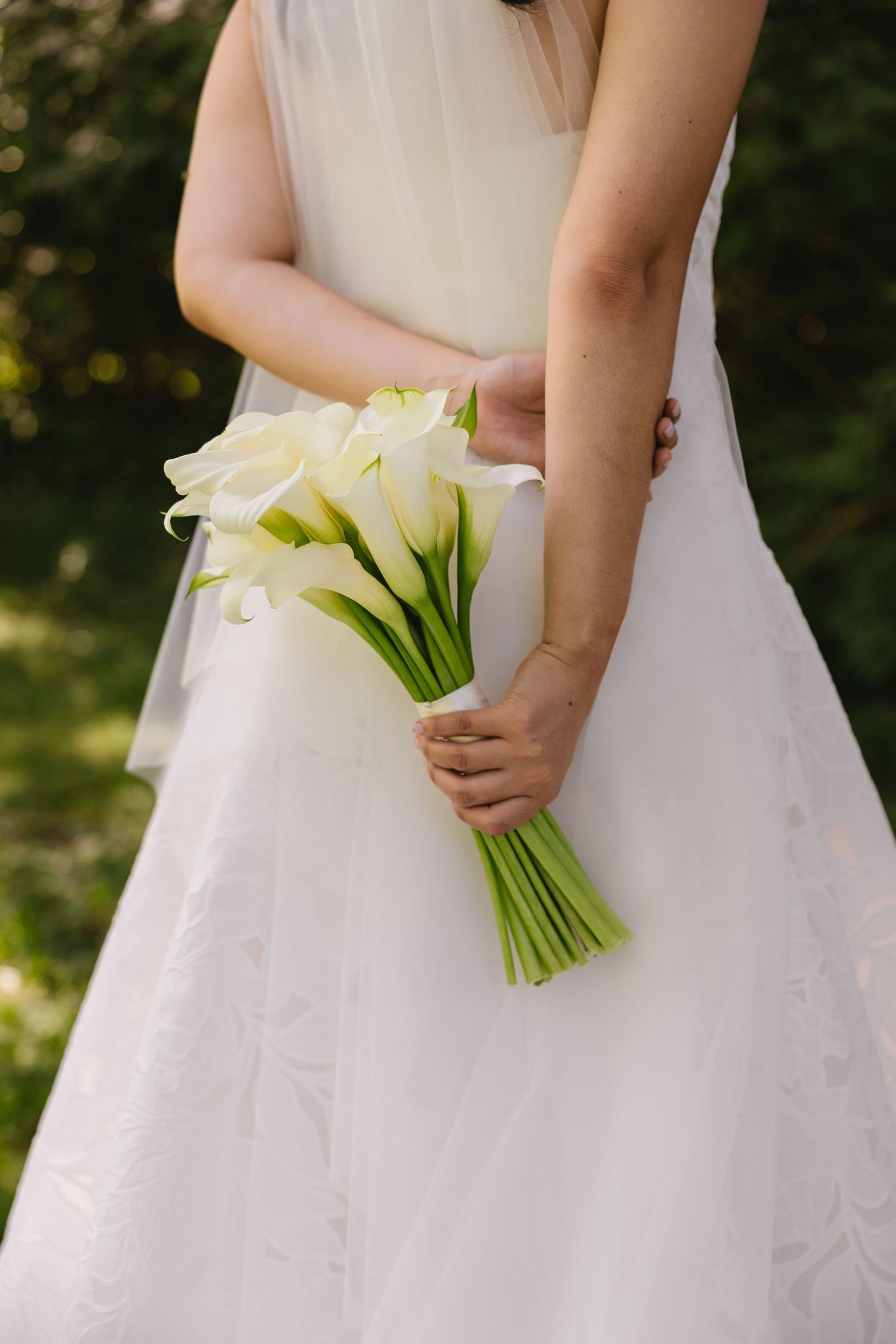 Close-up of bride holding a bouquet of white calla lilies behind her back at Wadsworth Homestead in Geneseo, NY.