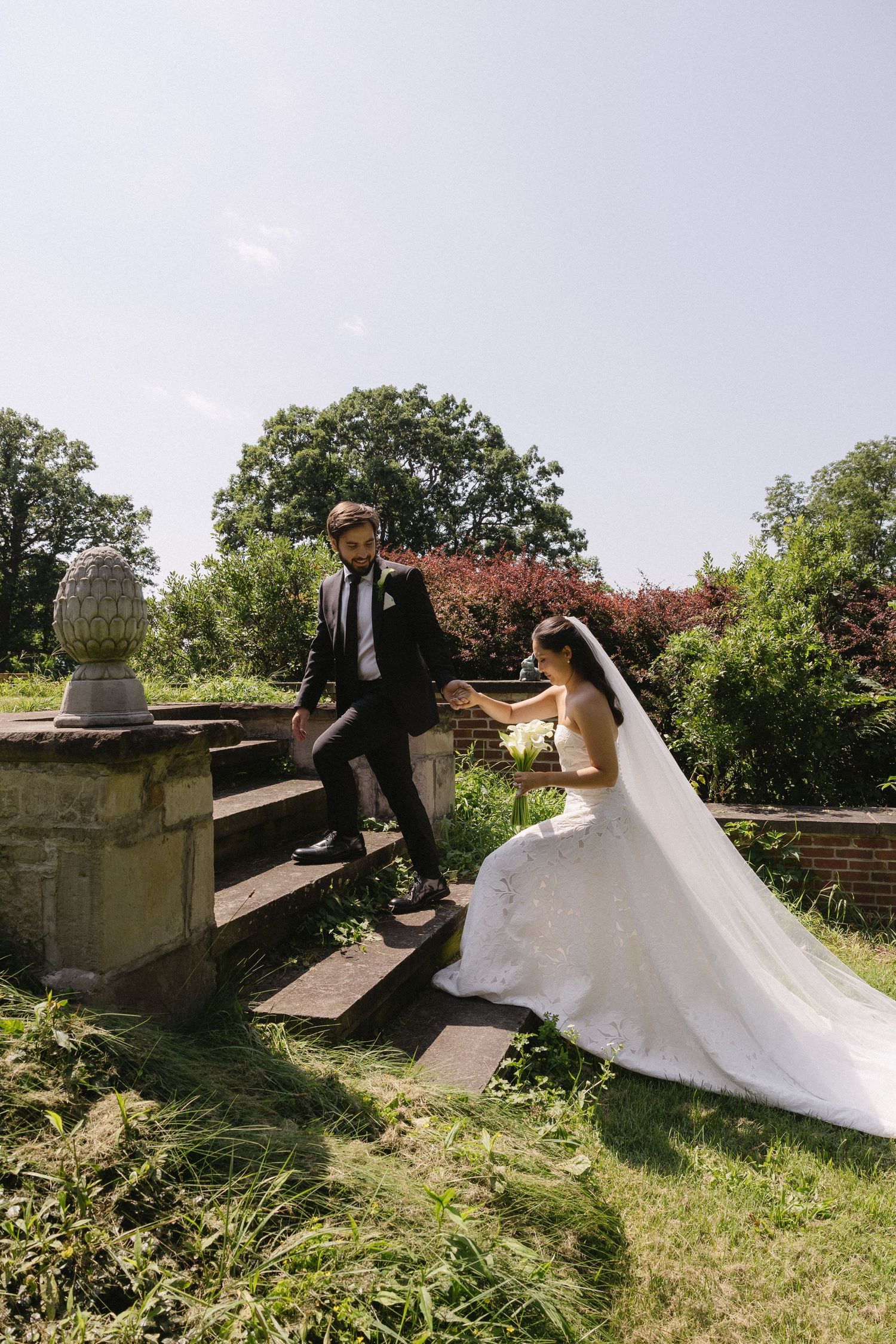 Bride and groom holding hands while walking up stone steps in a garden at Wadsworth Homestead in Geneseo, NY.