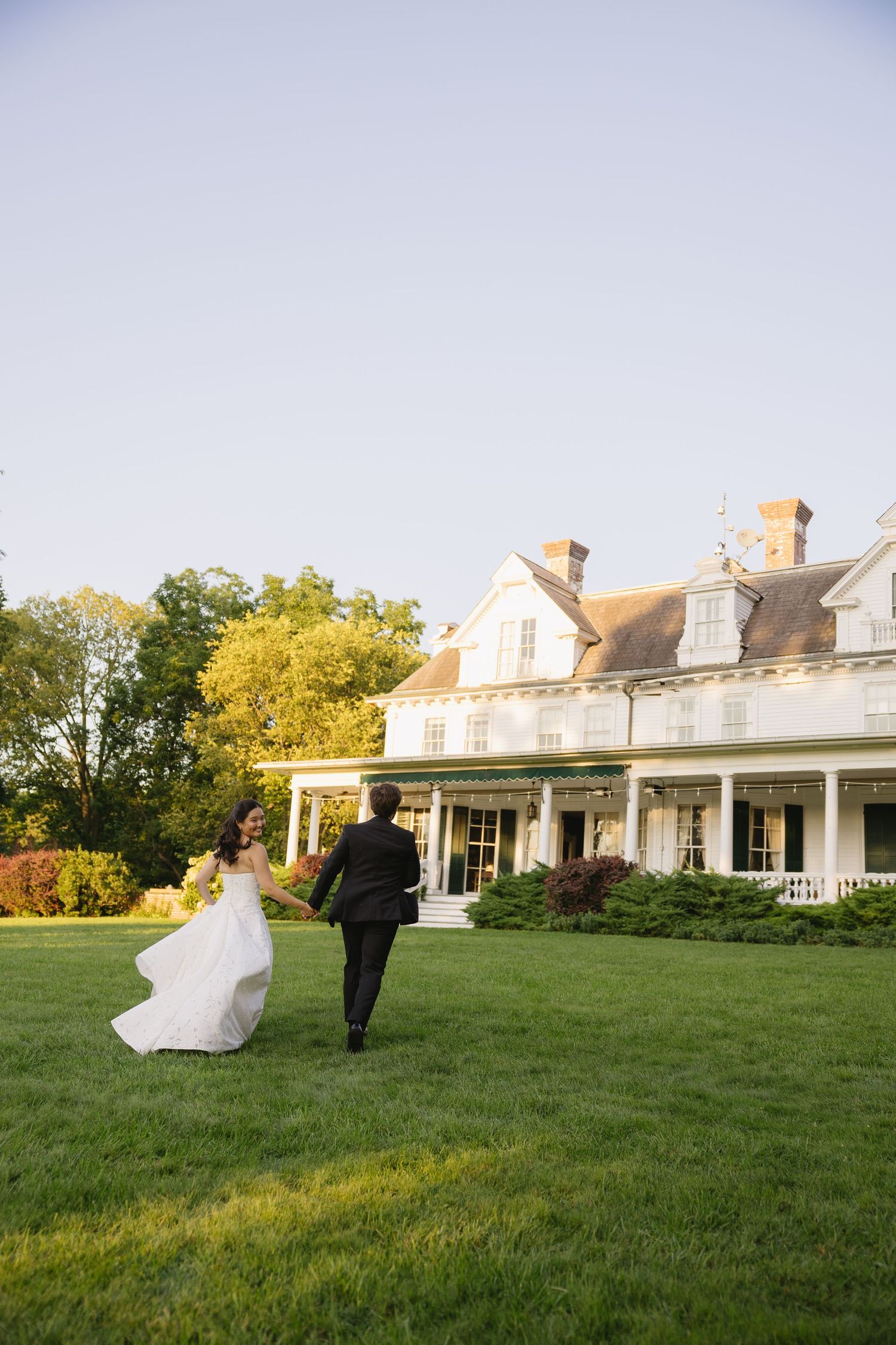 Bride and groom running towards Wadsworth Homestead in Geneseo, NY at golden hour, captured by a Upstate NY wedding photographer.