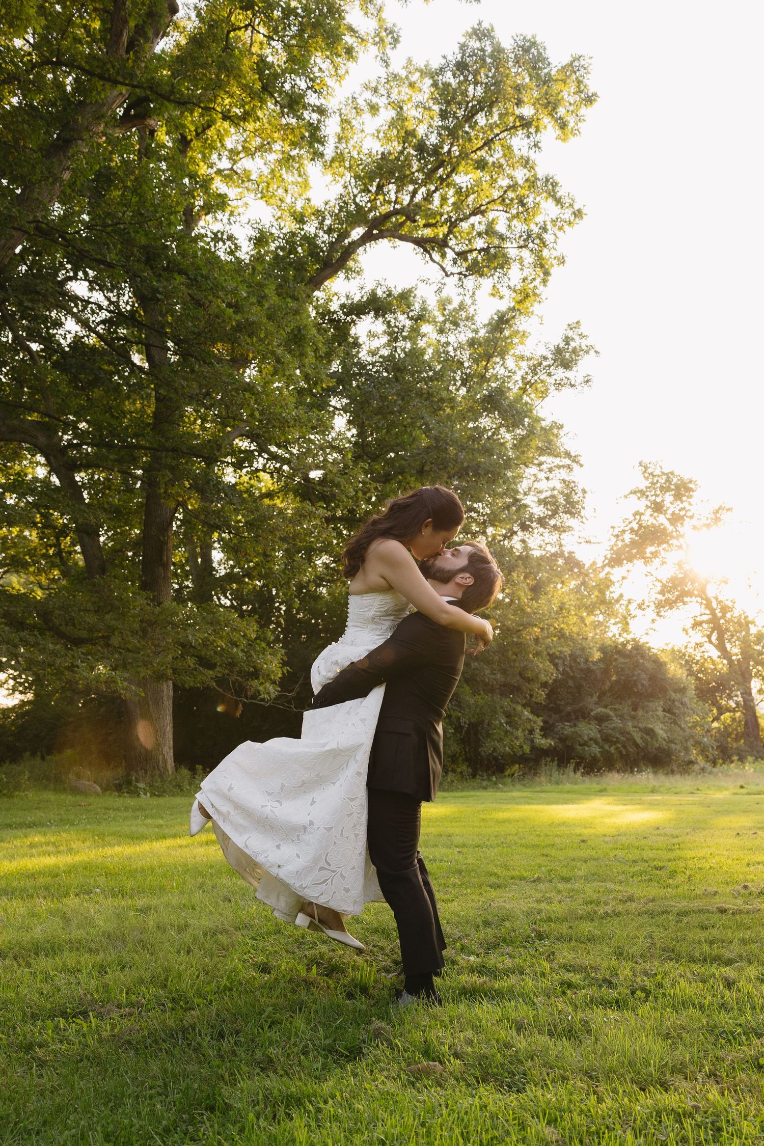 Groom lifting and kissing bride in a sunlit field at Wadsworth Homestead wedding venue in Geneseo, NY.