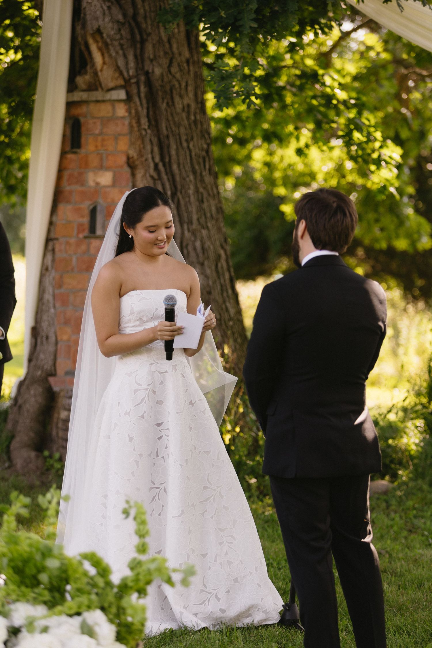 Bride reading vows into a microphone to the groom during outdoor ceremony at Wadsworth Homestead in Geneseo, NY.
