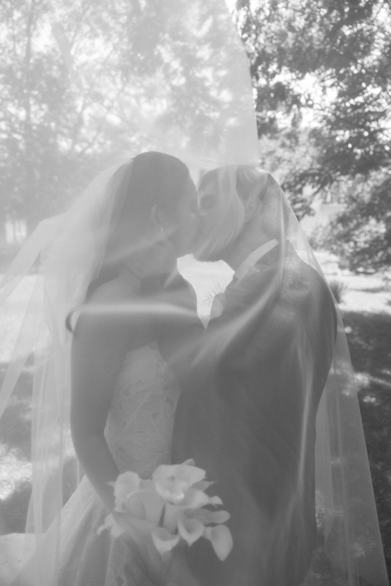 Black and white shot of bride and groom kissing beneath the wedding veil outdoors at Wadsworth Homestead in Geneseo, NY.