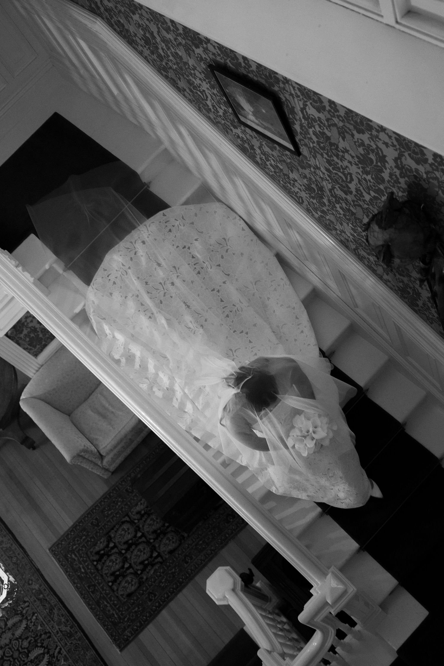 High-angle black and white shot of bride walking down staircase with long train and veil at Wadsworth Homestead in Geneseo, NY.