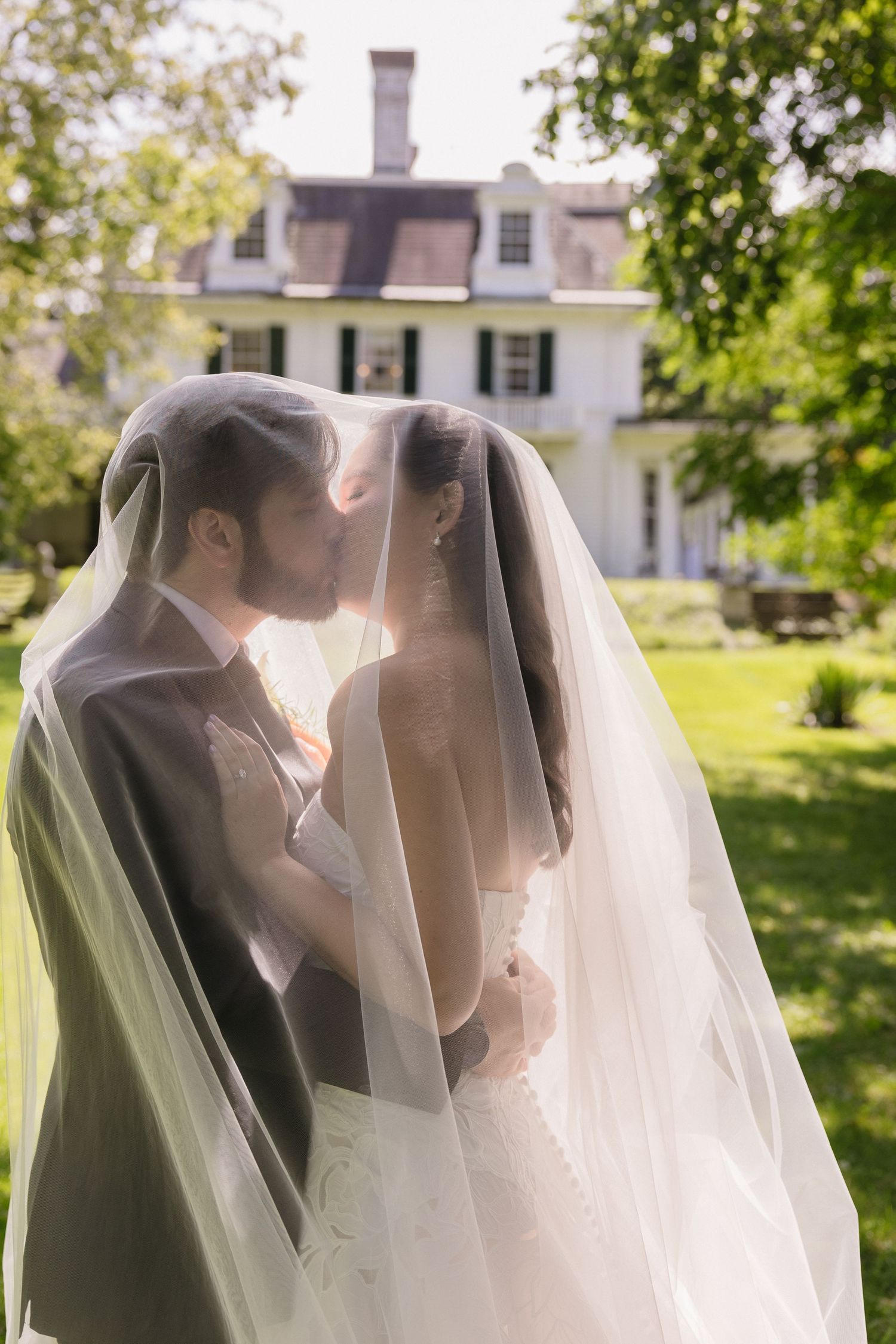 Bride and groom kissing beneath the wedding veil in a backlit outdoor setting at Wadsworth Homestead in Geneseo, NY.