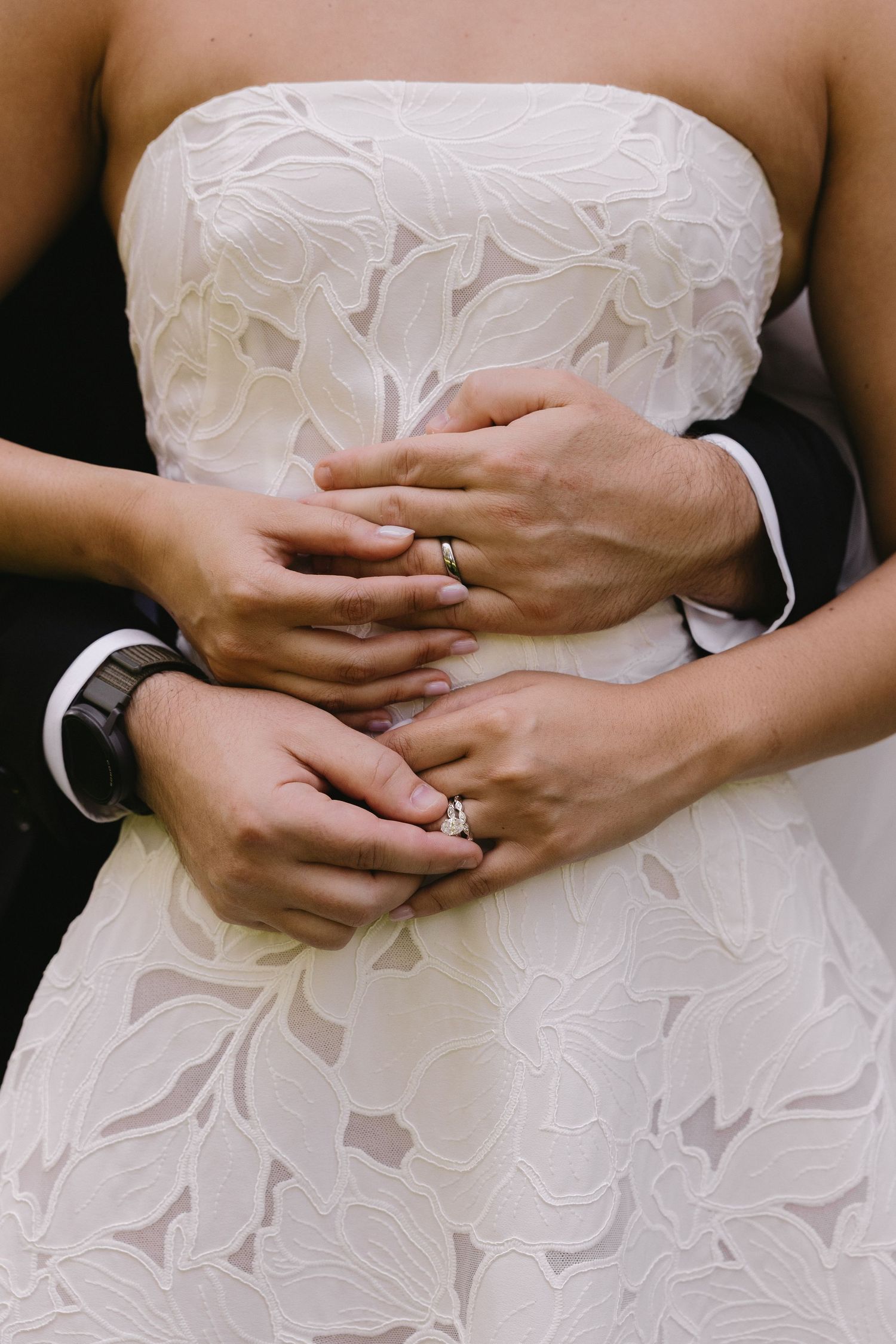 Close-up of bride and groom holding hands around bride's waist, showcasing their wedding rings at Wadsworth Homestead in Geneseo, NY.