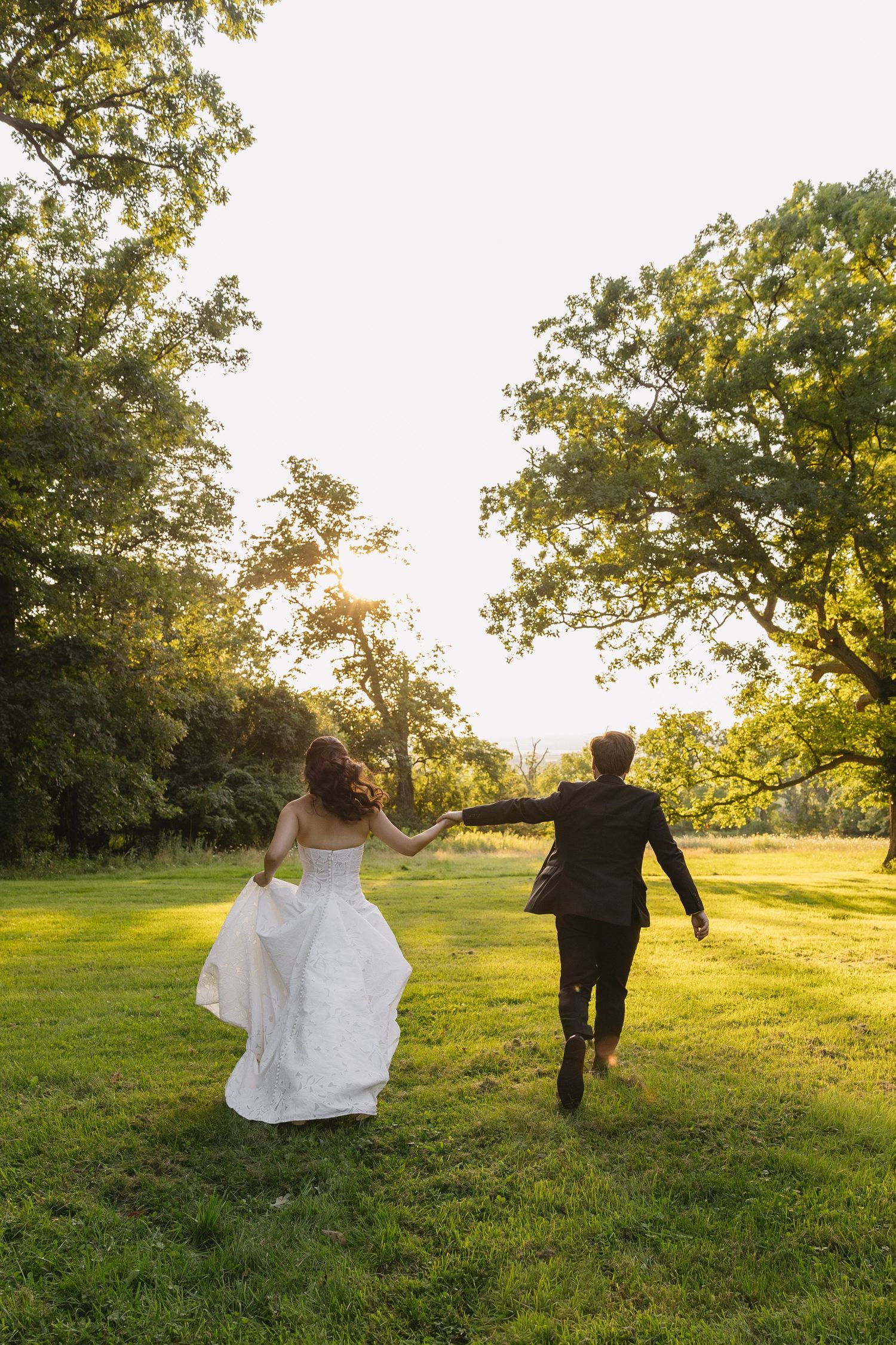 Bride and groom running hand in hand through a grassy field at sunset at Wadsworth Homestead in Geneseo, NY.