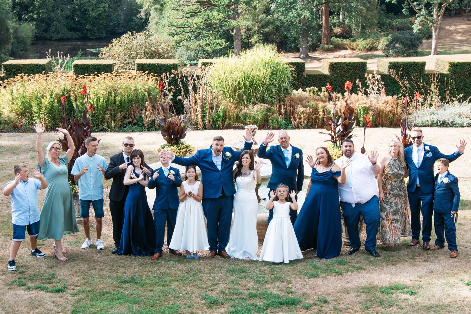 Wedding party in navy blue attire celebrating outdoors in a garden, with bride in white gown and guests cheering.