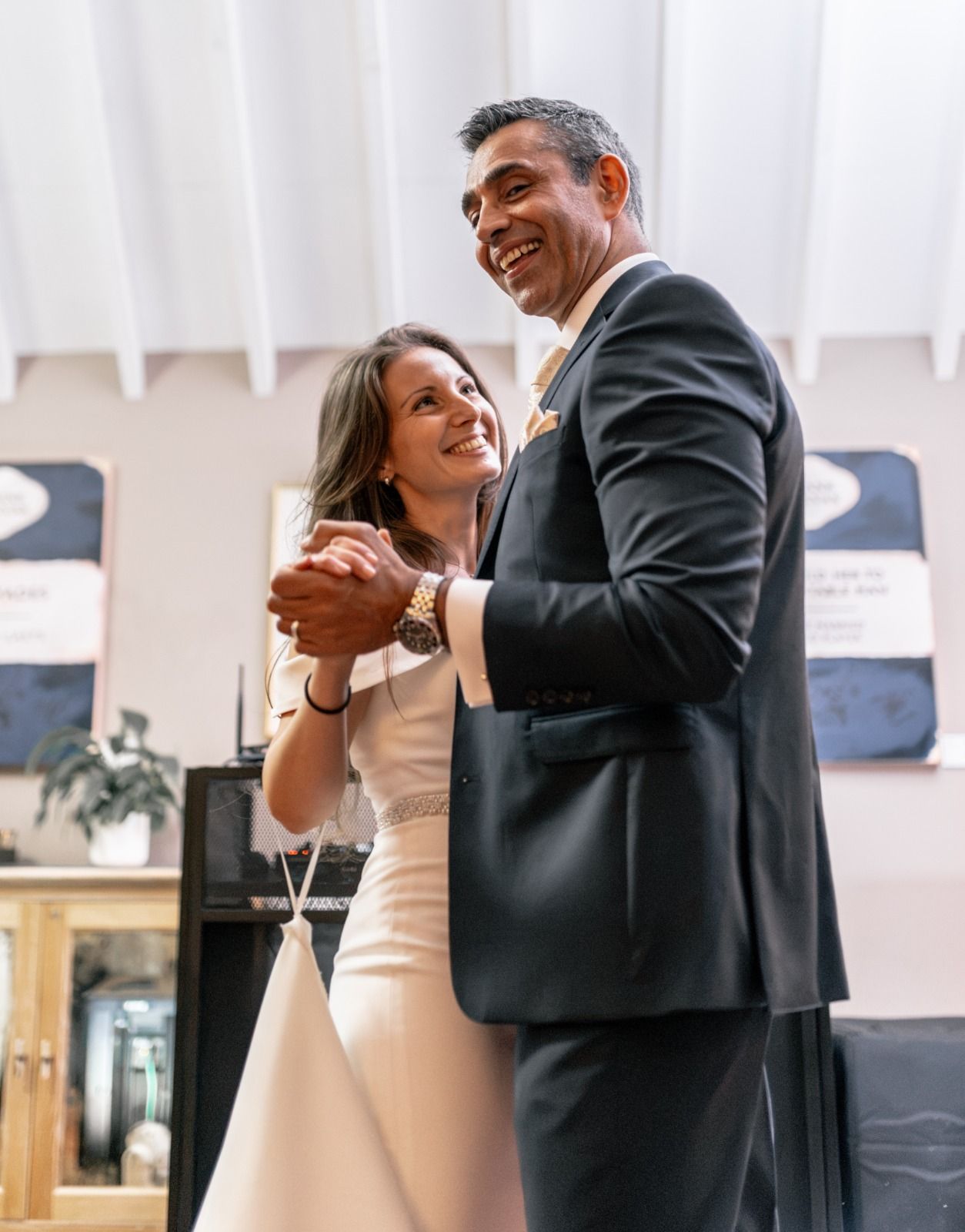A joyful couple shares their first dance at their wedding, with the bride in white and groom in a dark suit.
