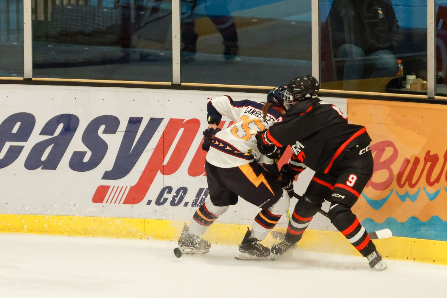 Two ice hockey players compete for puck along the boards with easyprint.co.uk advertising banner visible in background.