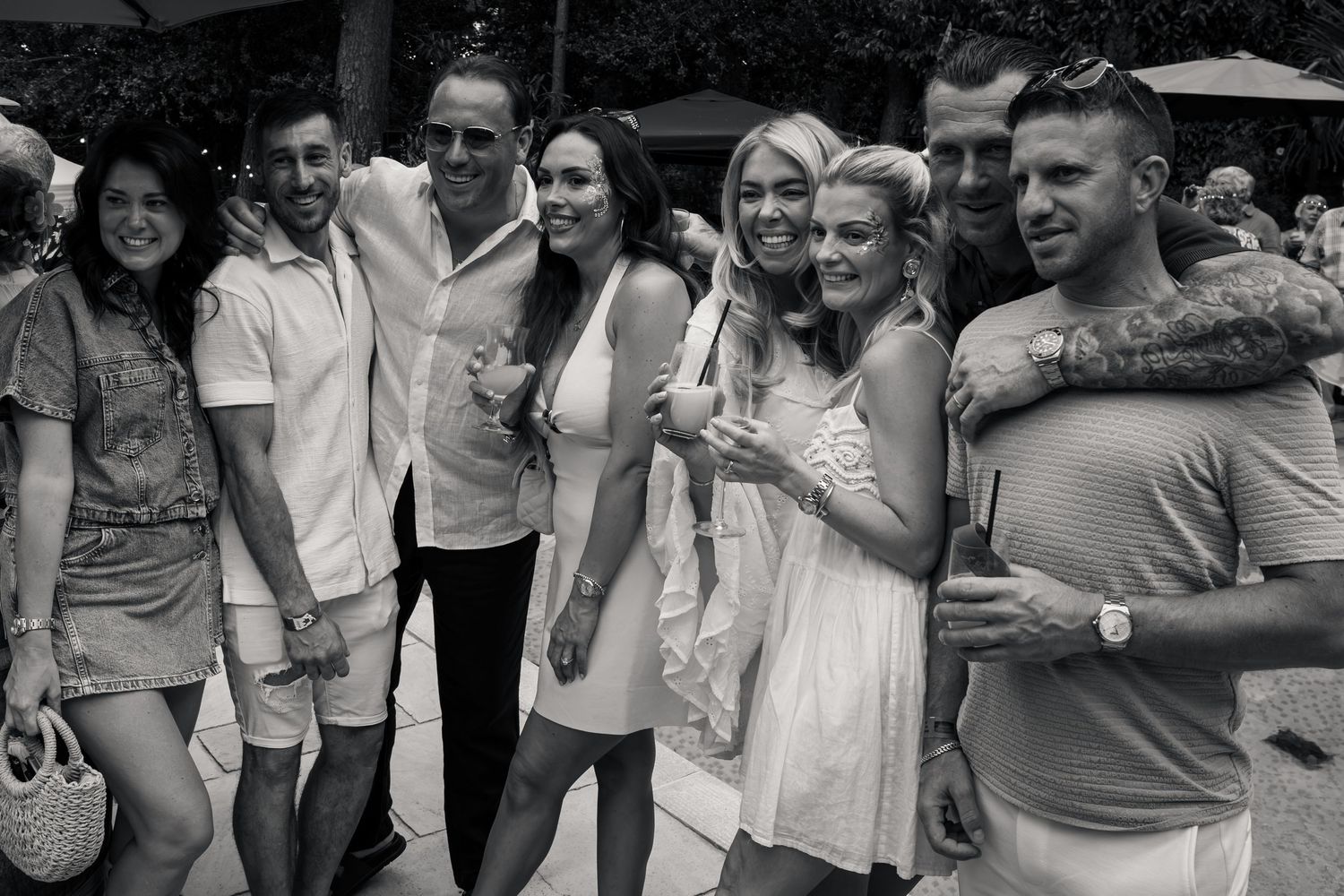 A group of seven smiling adults pose together at an outdoor summer party in a black and white photo.