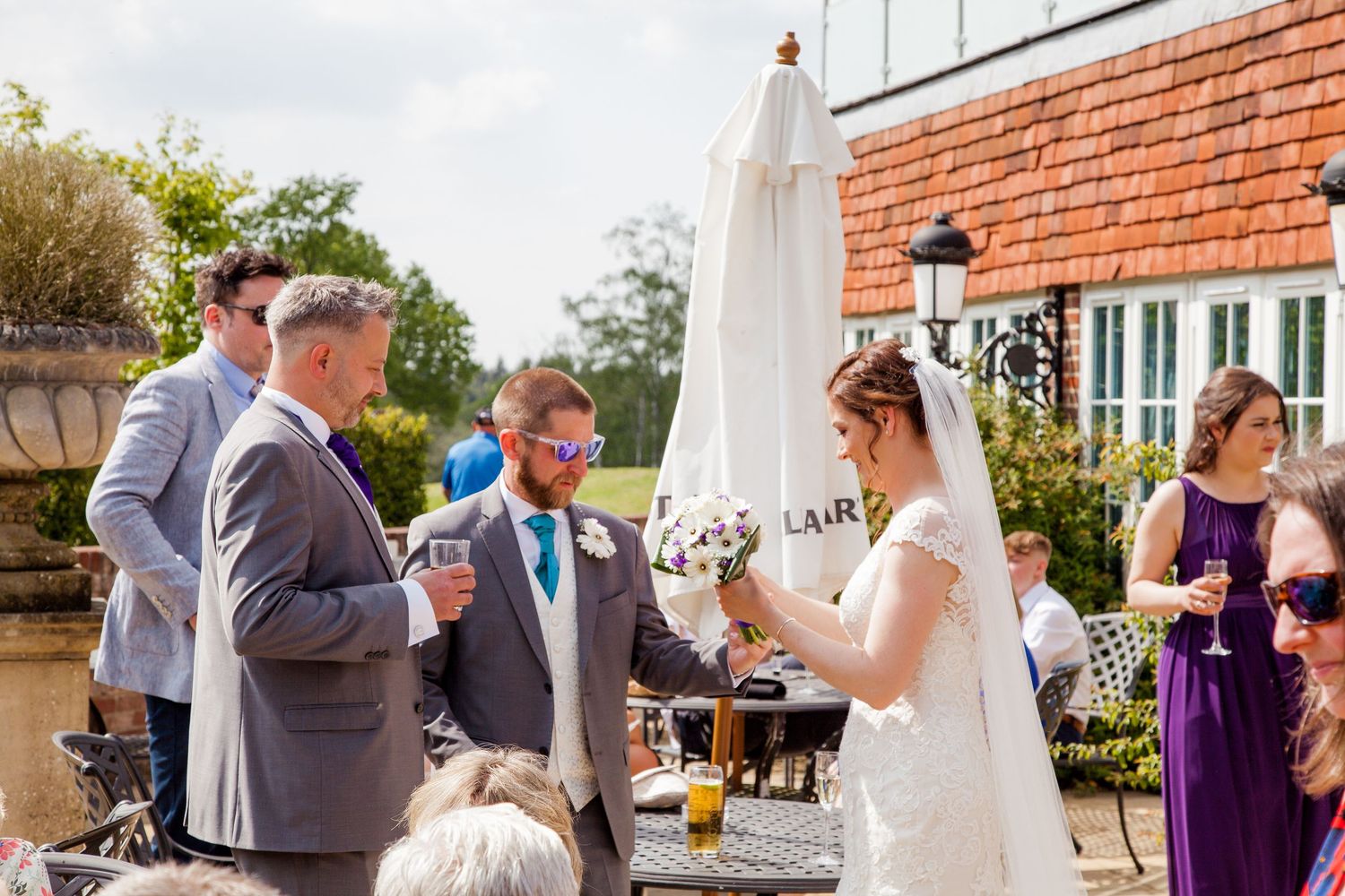 Bride and groom exchanging vows outdoors at a sunny wedding ceremony with guests watching.