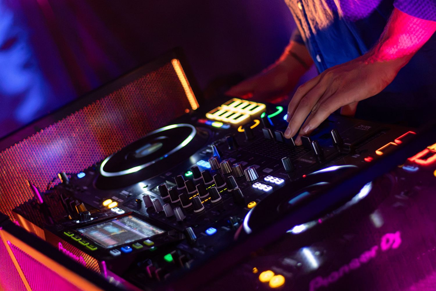 DJ hands mixing music on professional turntable controller with colorful neon lights.