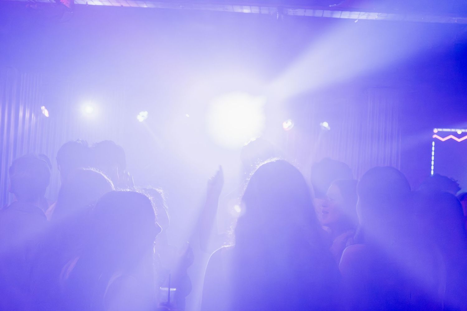 Crowd of silhouettes dancing under bright purple and blue stage lights at a concert.