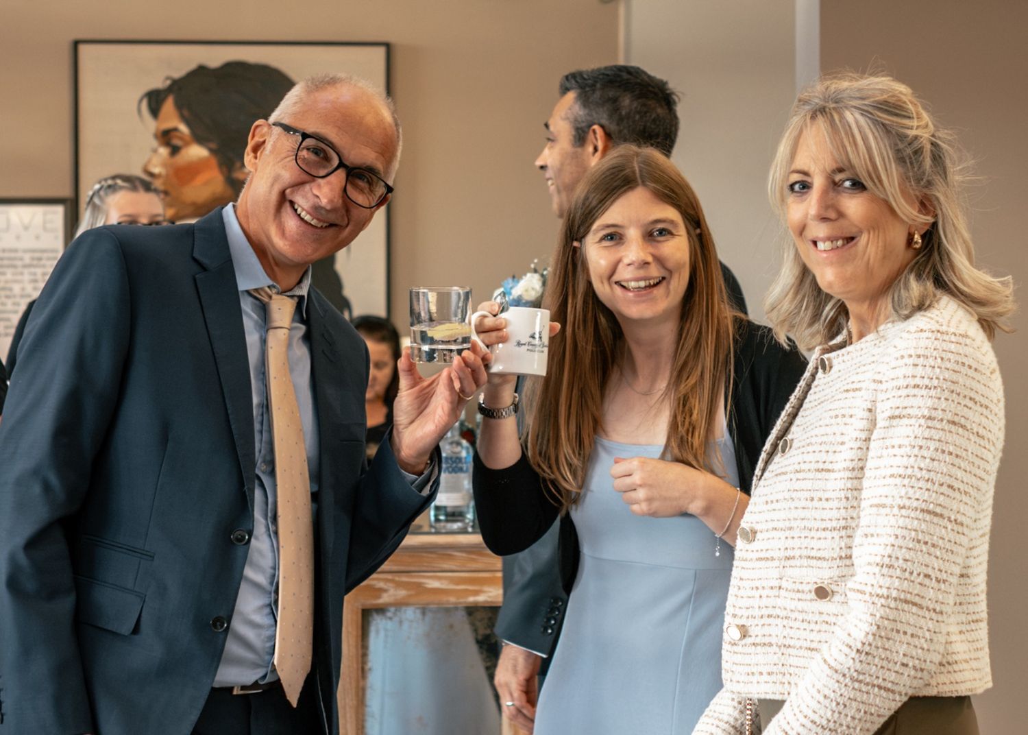 Three professionals smiling and toasting with drinks at a corporate networking event indoors.