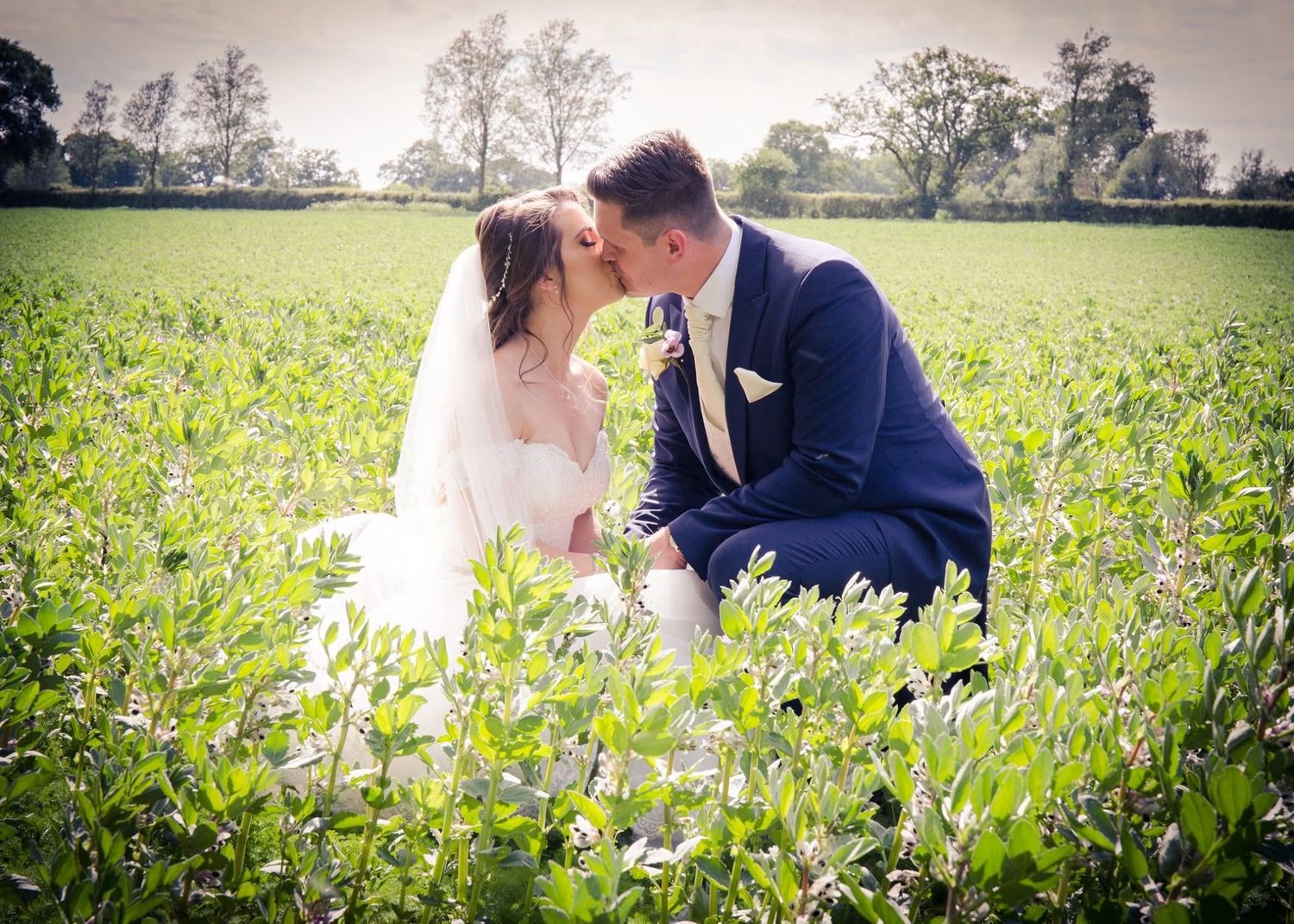 Bride and groom sharing romantic kiss in lush green field on their wedding day.