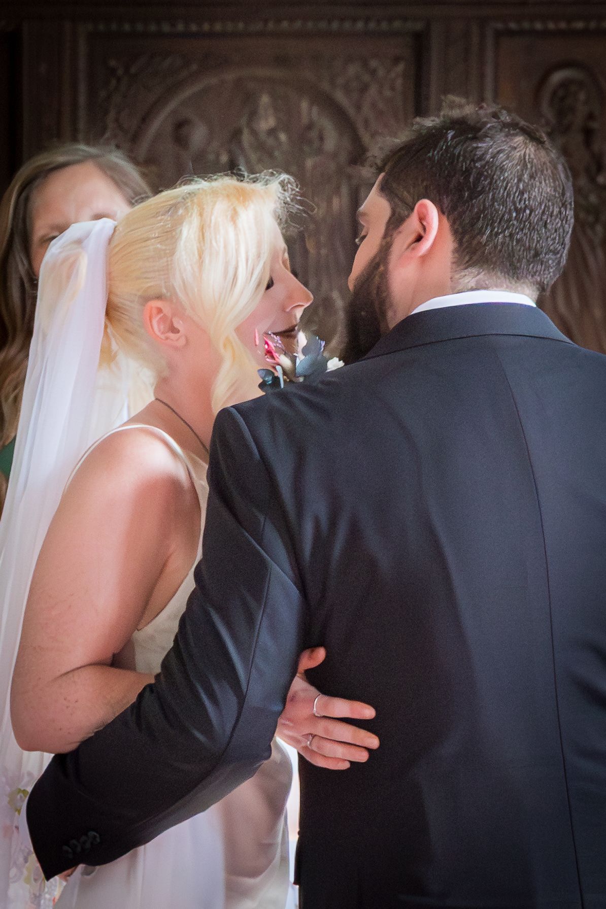 Bride in veil laughing with bearded groom during wedding ceremony indoors.