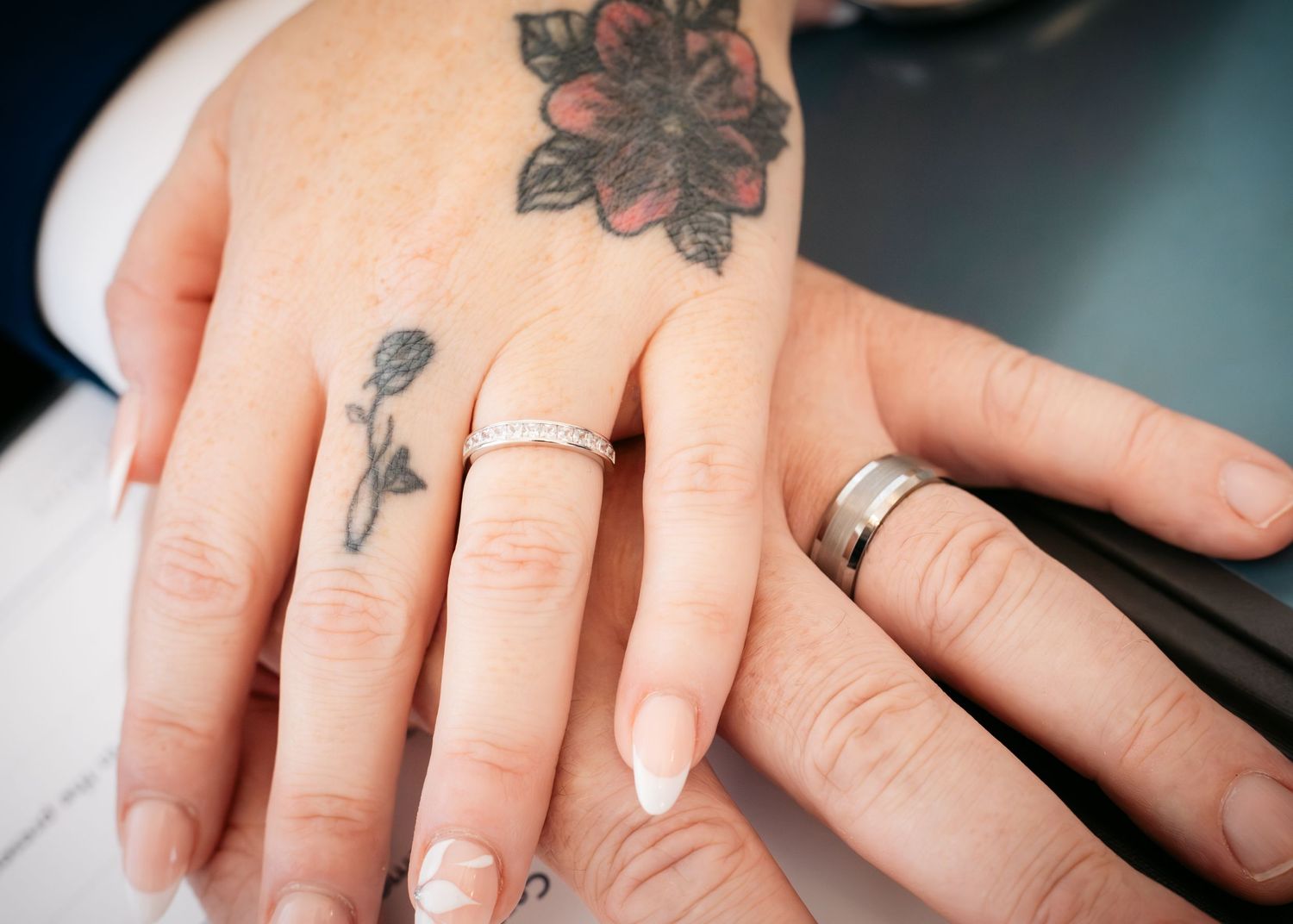 Close-up of two hands with wedding rings and floral tattoos, symbolizing a newly married couple.