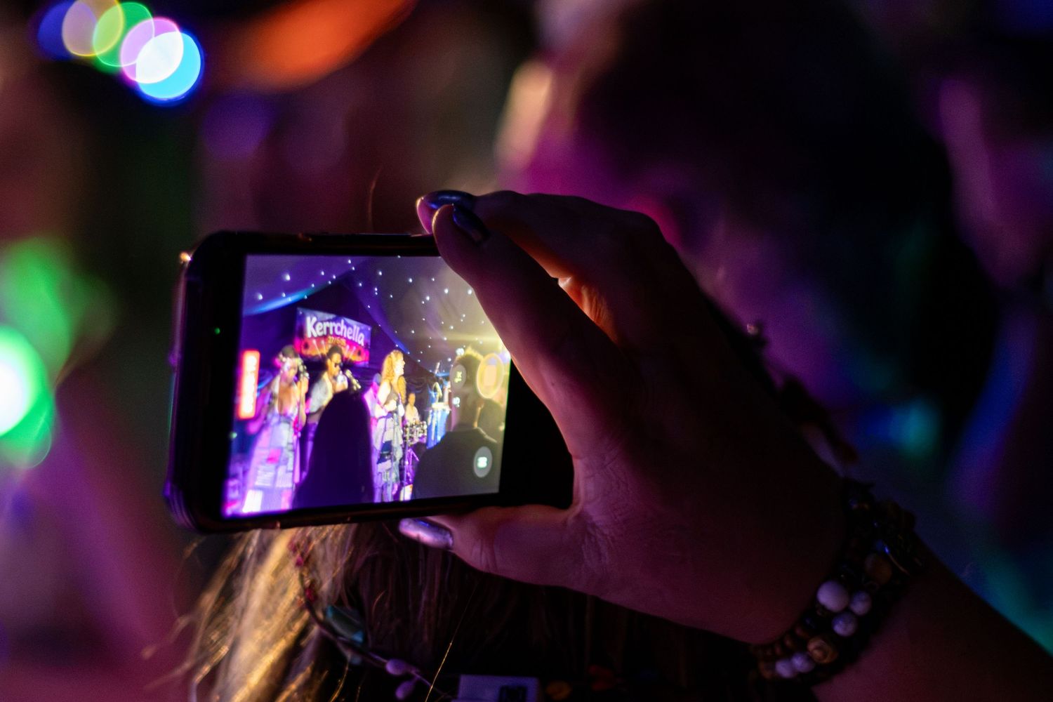 Concert attendee filming performers on stage with smartphone at colorful music festival.