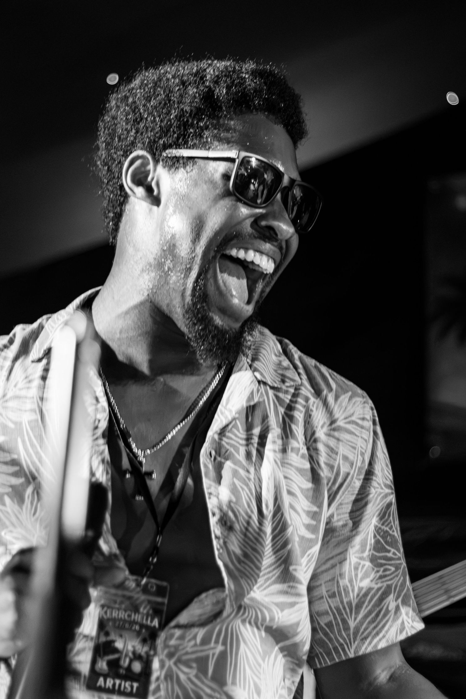 A joyful Black musician with sunglasses playing drums in black and white.