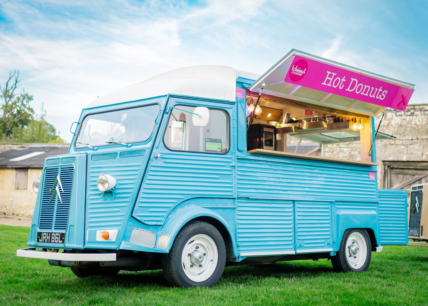 Vintage blue Citroen HY food truck serving hot donuts, parked on green grass under a blue sky.