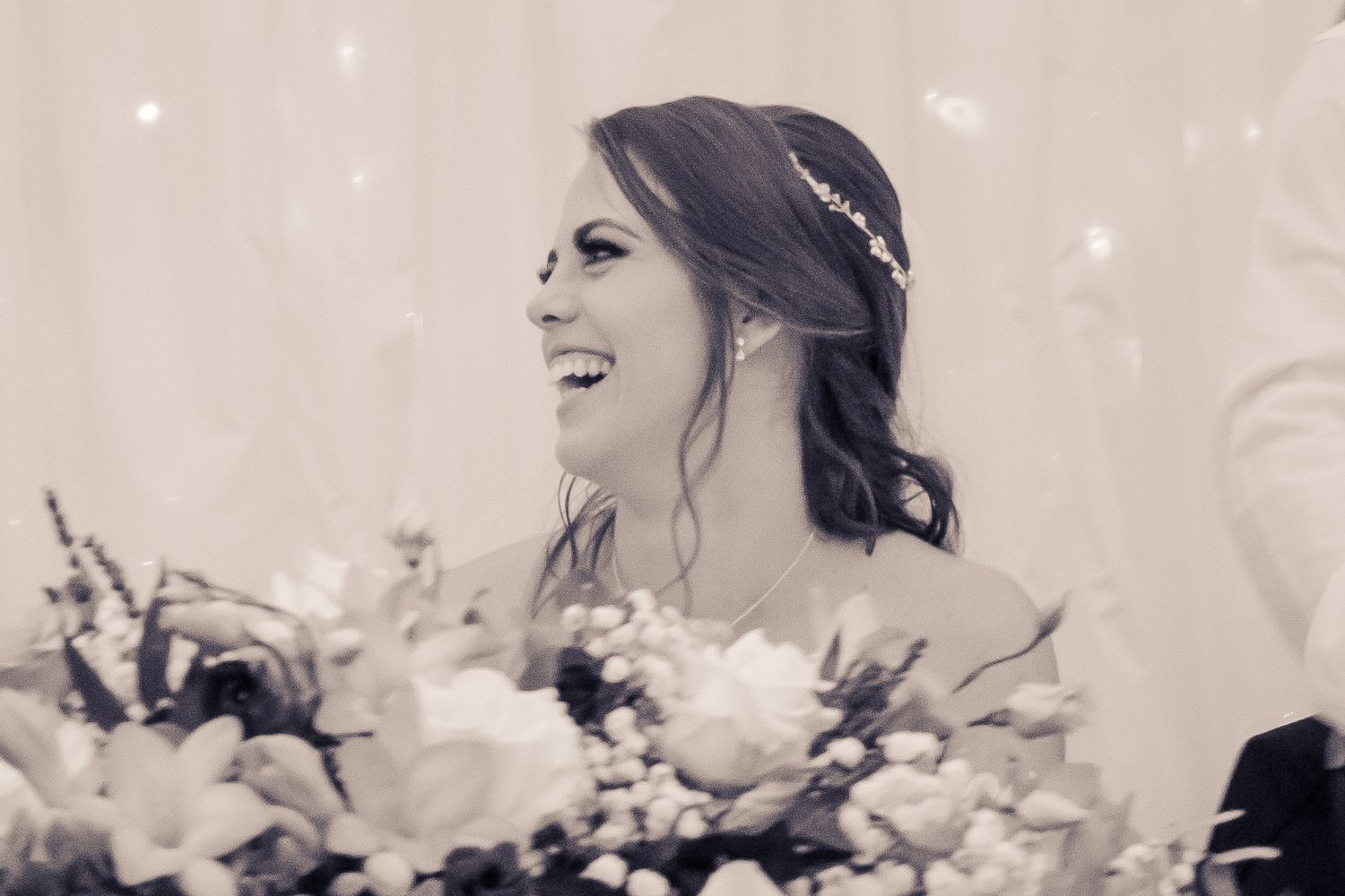 Radiant bride laughing joyfully with floral bouquet in black and white wedding photo.