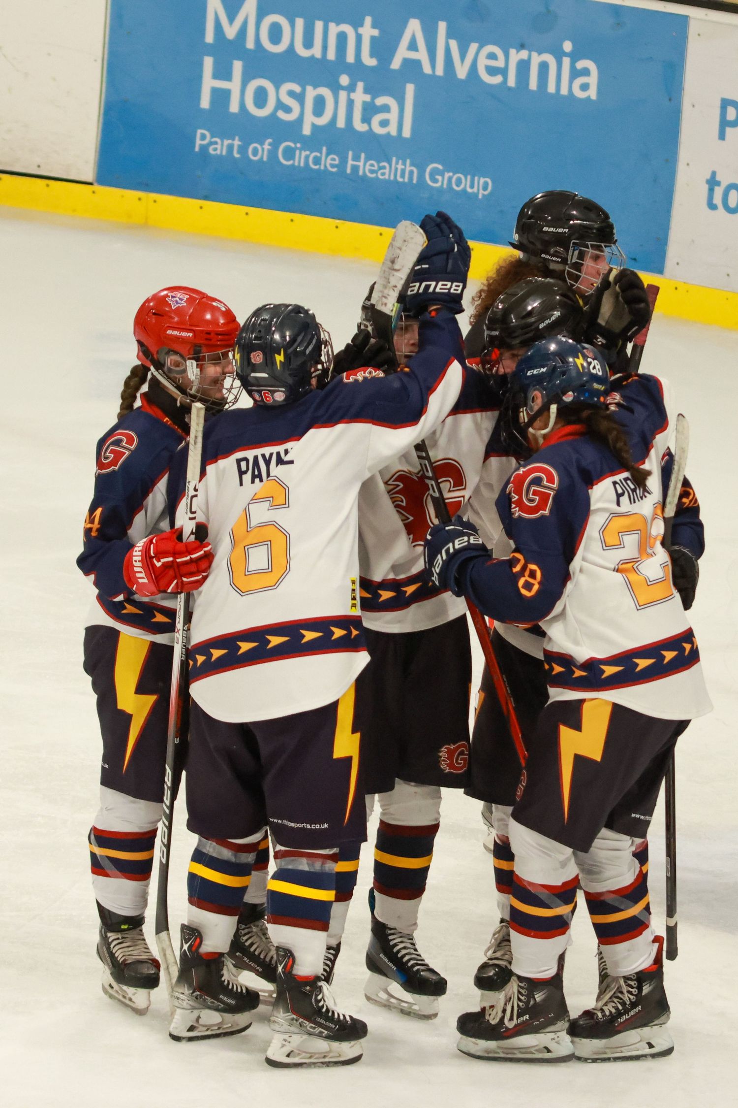 Ice hockey players in navy Guildford Flames uniforms celebrate a goal on the rink.
