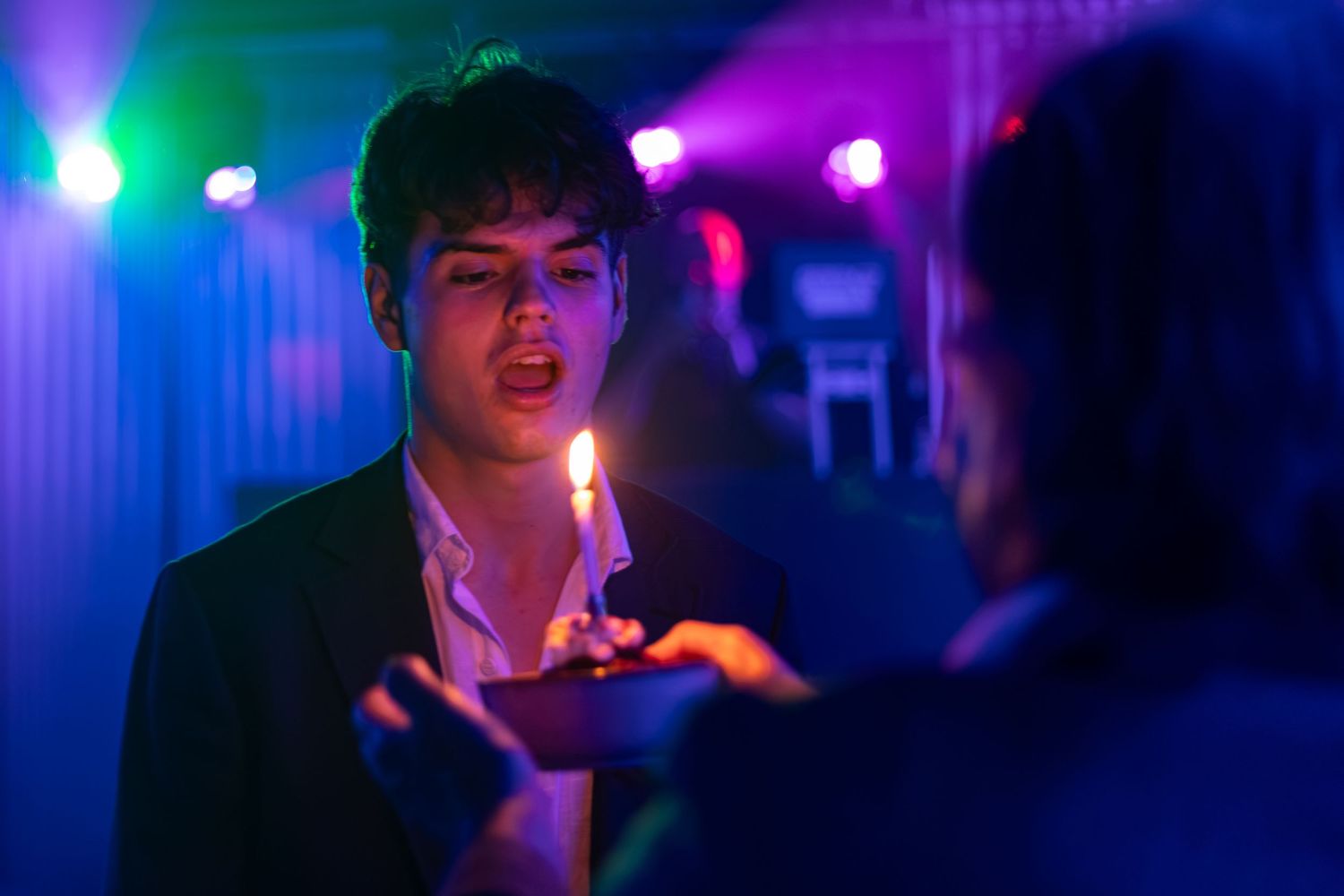 Young man getting cigarette lit under colorful neon lights at a nightclub party.