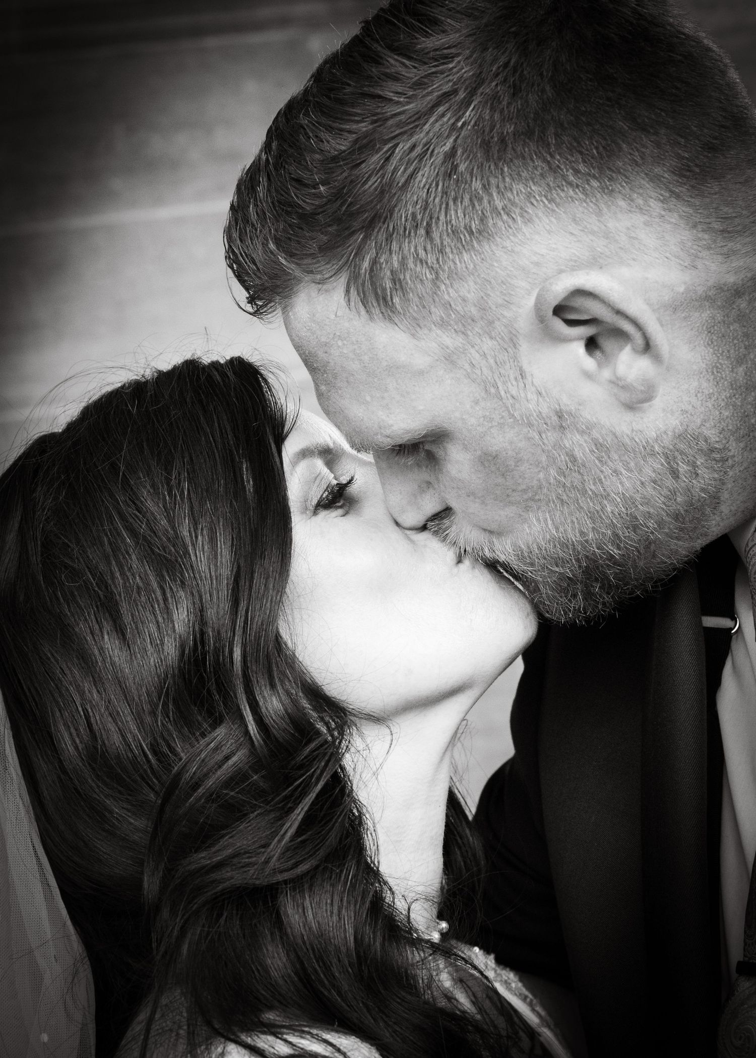 Black and white romantic photo of a couple sharing a tender kiss, woman with dark wavy hair and man with short gray hair.