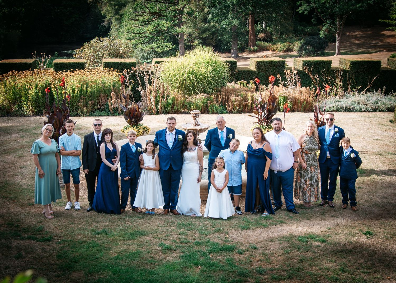 Wedding party poses in a lush garden, bride and groom surrounded by family in blue formal attire.