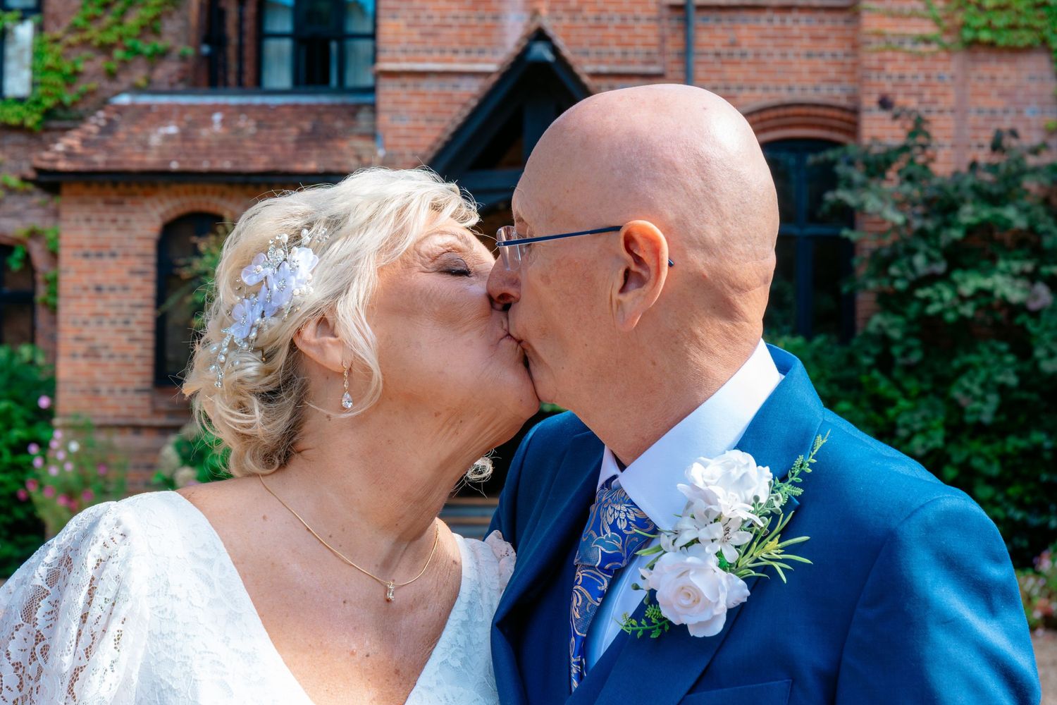 Bride and groom sharing a romantic kiss outdoors at a brick manor wedding venue on a sunny day.