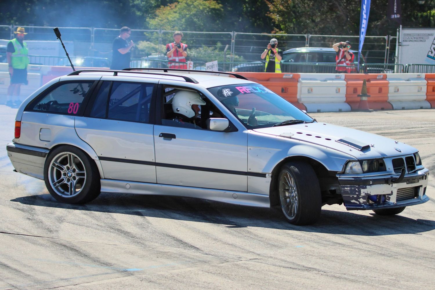Silver BMW E36 touring wagon drift car with damaged front end competing at an outdoor event.