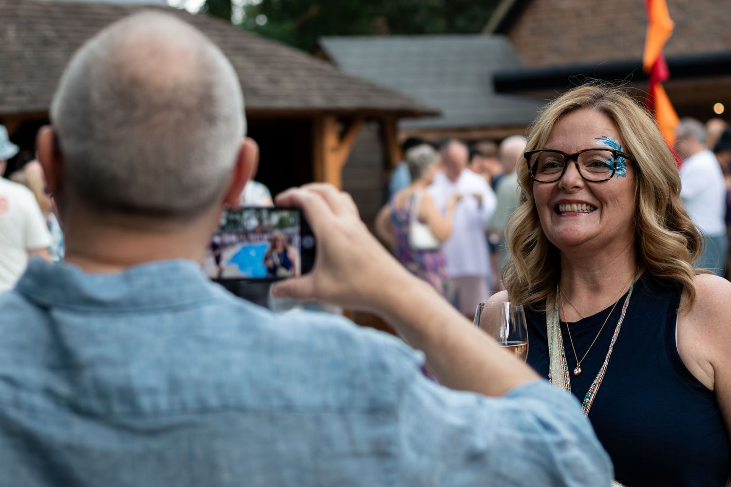 A smiling woman with glasses poses for a photo at an outdoor social gathering event during daytime.