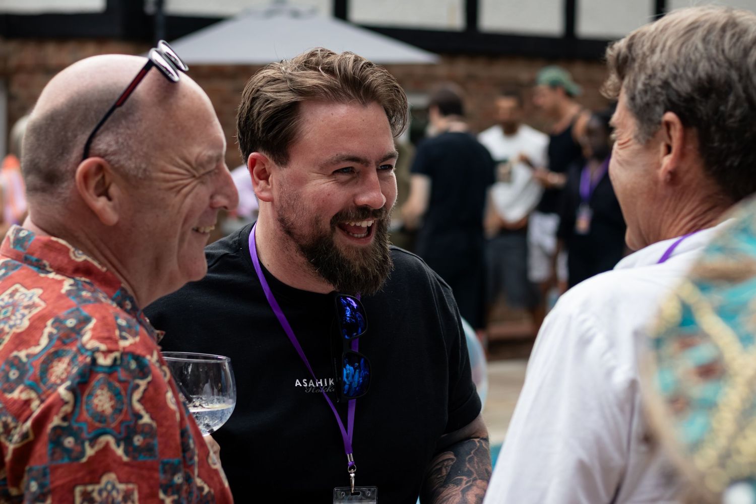 Three men smiling and socializing outdoors at a casual summer gathering event.