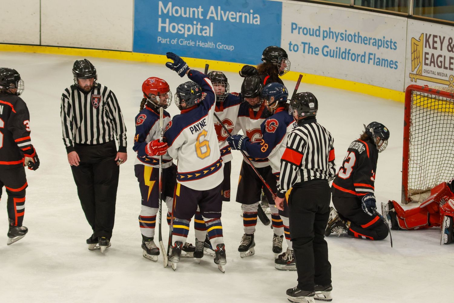 Ice hockey players from Guildford Flames and opponents converge near the goal during an intense match.