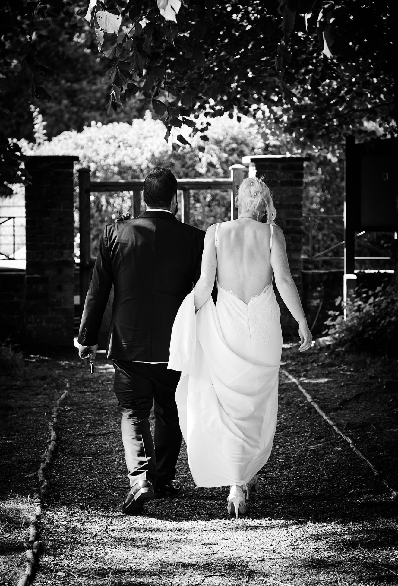 Black and white photo of bride and groom walking hand in hand outdoors.