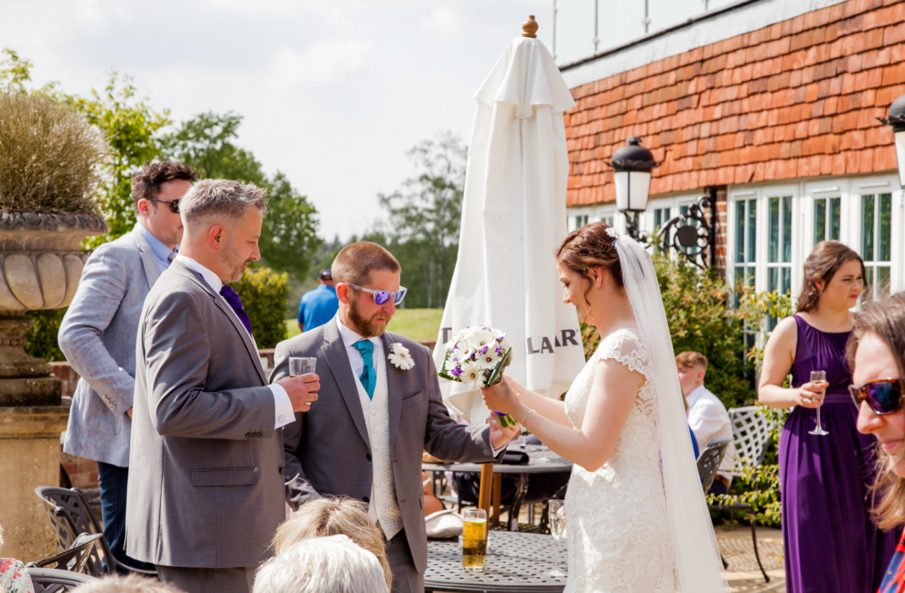 Wedding guests toasting with champagne glasses outside elegant venue on sunny day.