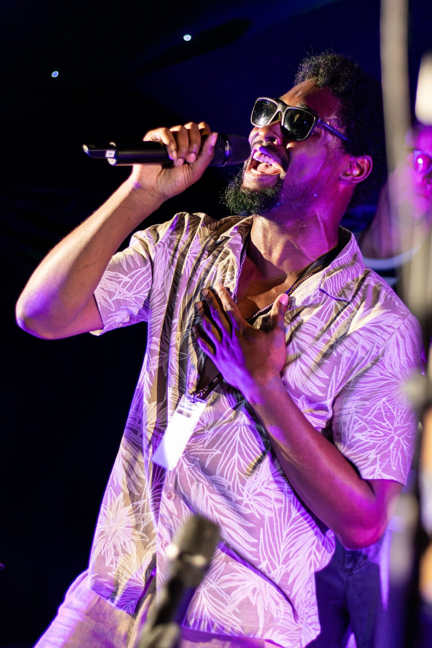 A Black male singer performing passionately on stage under purple lights.