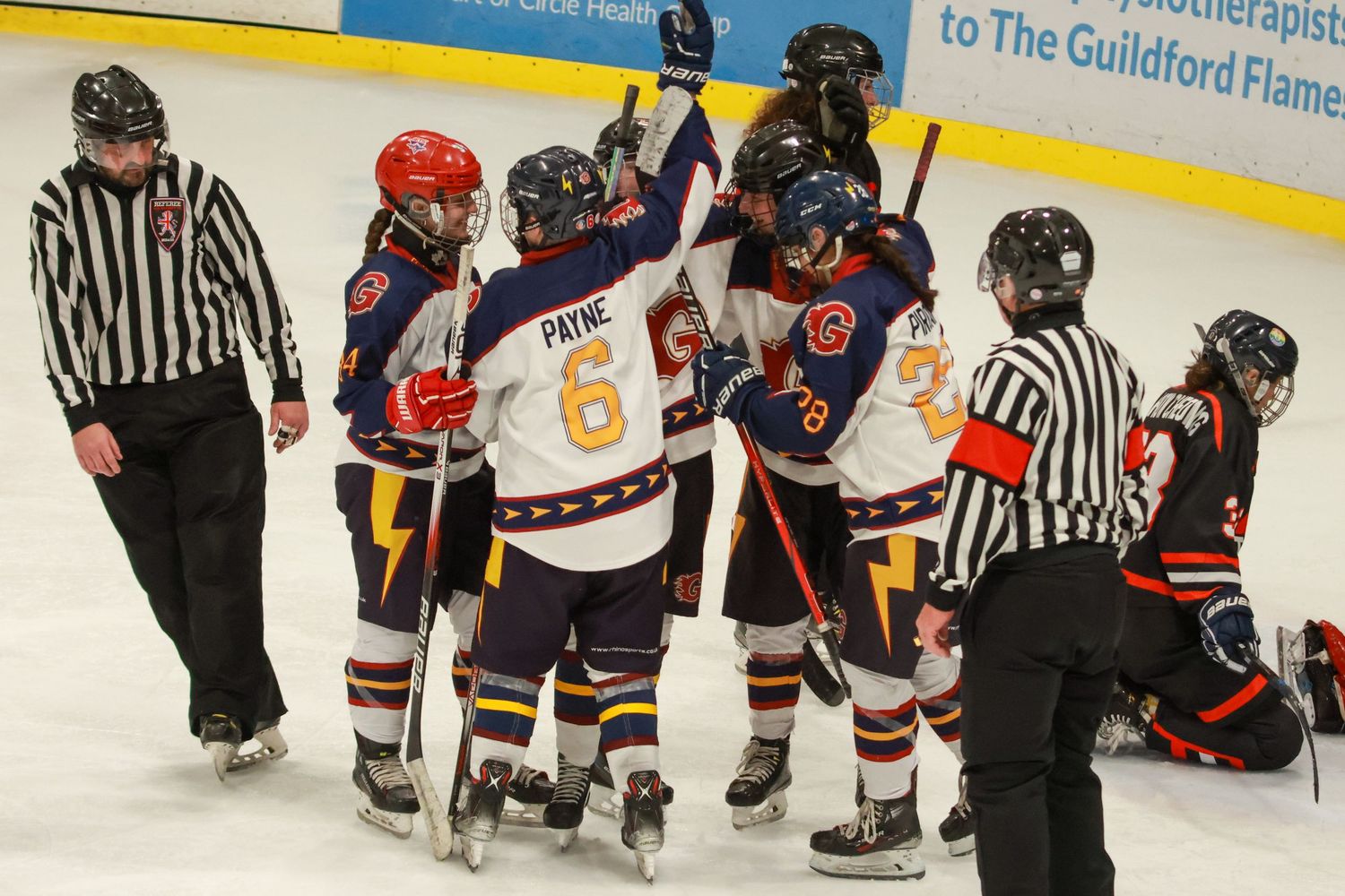 Guildford Flames players celebrate on ice as a referee and fallen opponent are visible nearby.