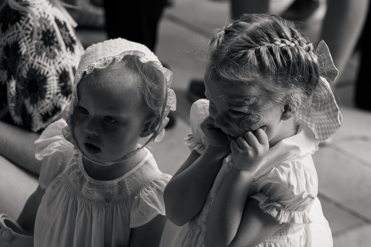 Black and white photo of two young flower girls in white dresses and bonnets.