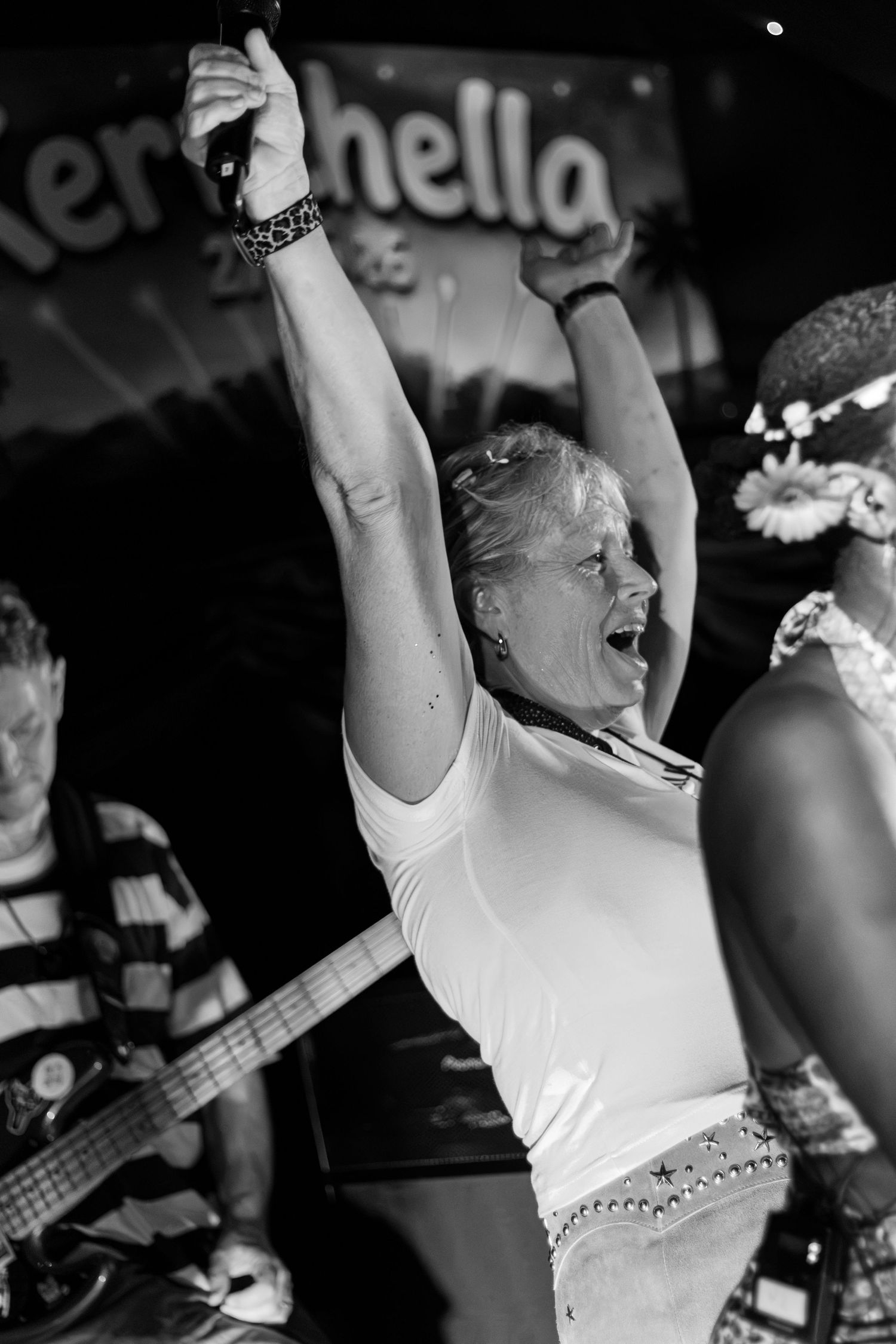 A woman raising both arms triumphantly on stage at a music festival.